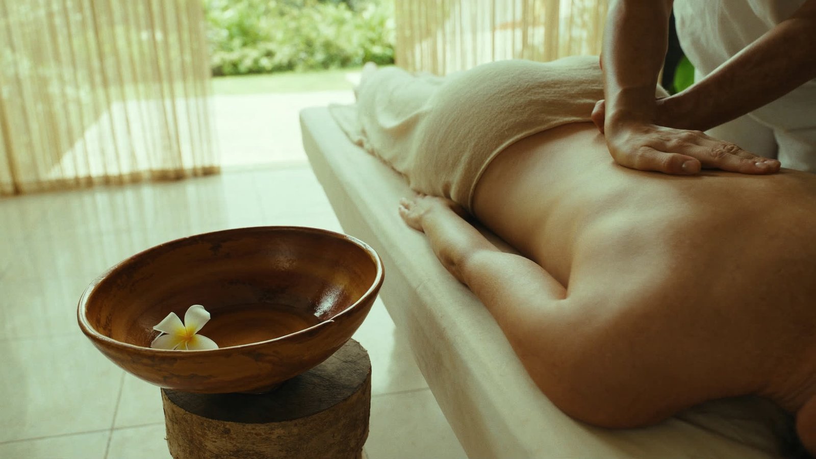 Hands working along a shoulder during a Balinese massage in an open-sided pavilion.